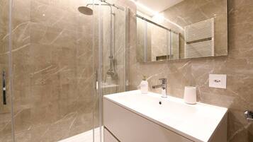 A modern bathroom with a glass-enclosed shower, a white vanity with a mirror, and marble walls.