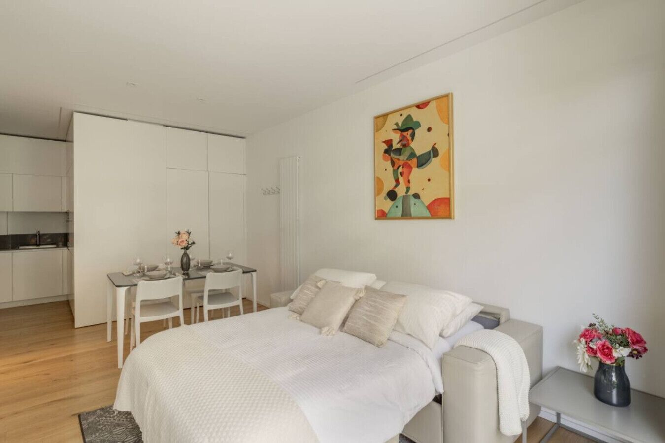 Ein modernes Schlafzimmer mit einem großen Bett, einem Esstisch und einer Küche im Hintergrund.