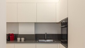 Une cuisine moderne avec des meubles blancs, un plan de travail noir, un évier en acier inoxydable, une machine à café rouge et un four noir.