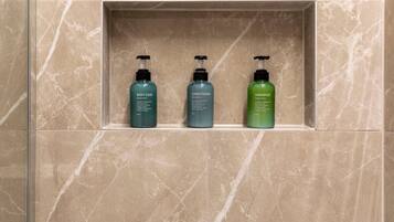 A bathroom with a marble wall and a shelf containing three bottles of toiletries: body soap, conditioner, and shampoo.