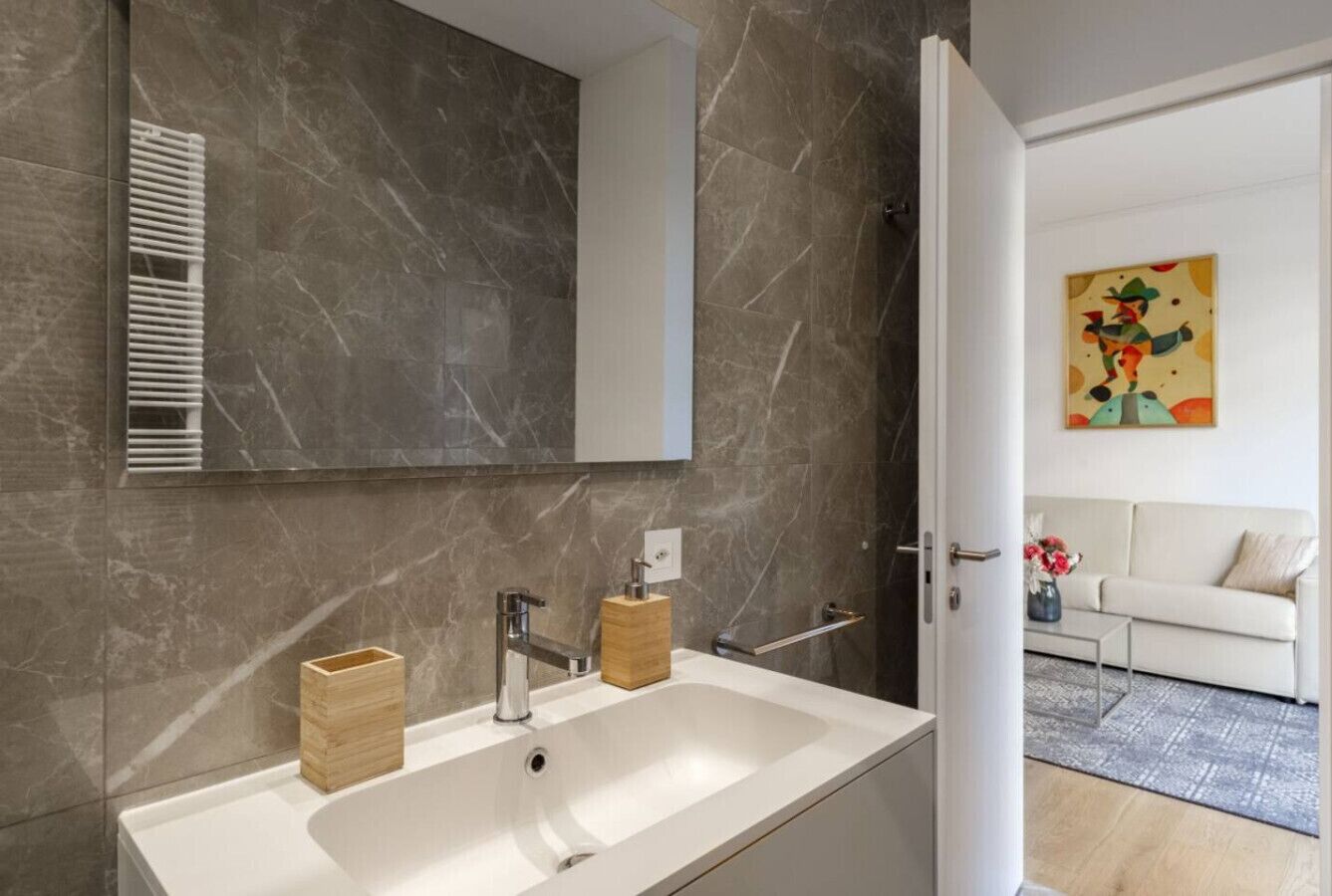 Une salle de bain moderne avec un grand miroir, un lavabo blanc et un porte-savon en bois.