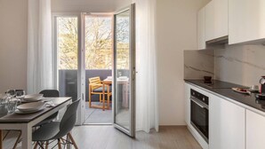 A modern kitchen with a dining area and a sliding glass door leading to a balcony with a view of trees.