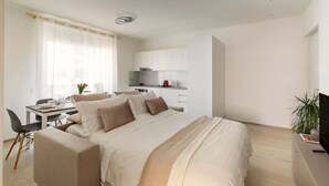 A modern hotel room with a bed, a desk, and a kitchenette.