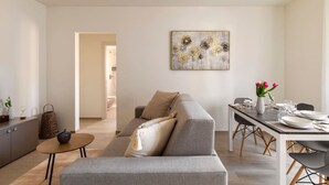 A modern living room with a grey sofa, a dining table set with plates and glasses, and a painting on the wall.