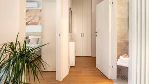 Een hal met een bed, een plant en een badkamer zichtbaar door een geopende deur.