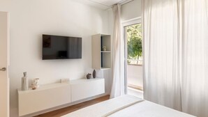Een moderne slaapkamer met een groot bed, een wandtelevisie, een ingebouwde bank met opbergruimte en uitzicht op de omgeving door een groot raam.