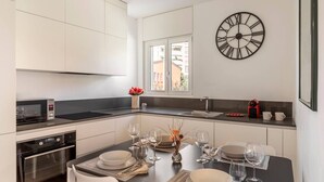 Een moderne keuken met witte kastjes, een inbouwoven, een magnetron en een eethoek voor vier personen, compleet met tafel, stoelen en wijnglazen.