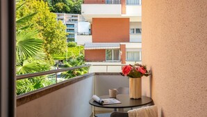 Een balkon met een tafel, een vaas met bloemen en uitzicht op een woongebied met bomen en gebouwen.