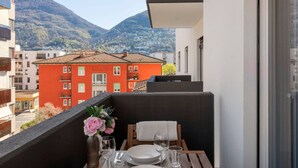 Un balcon avec une table dressée pour deux personnes, d’où l’on peut admirer un bâtiment rouge et des montagnes.