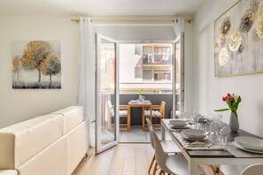 Ein modernes Wohnzimmer mit einer Couch, einem Esstisch für vier Personen und einem Balkon mit Tisch und Stühlen.