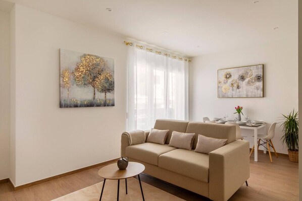 Ein Wohnzimmer mit einem beigen Sofa, einem kleinen runden Tisch und zwei Bildern an der Wand.