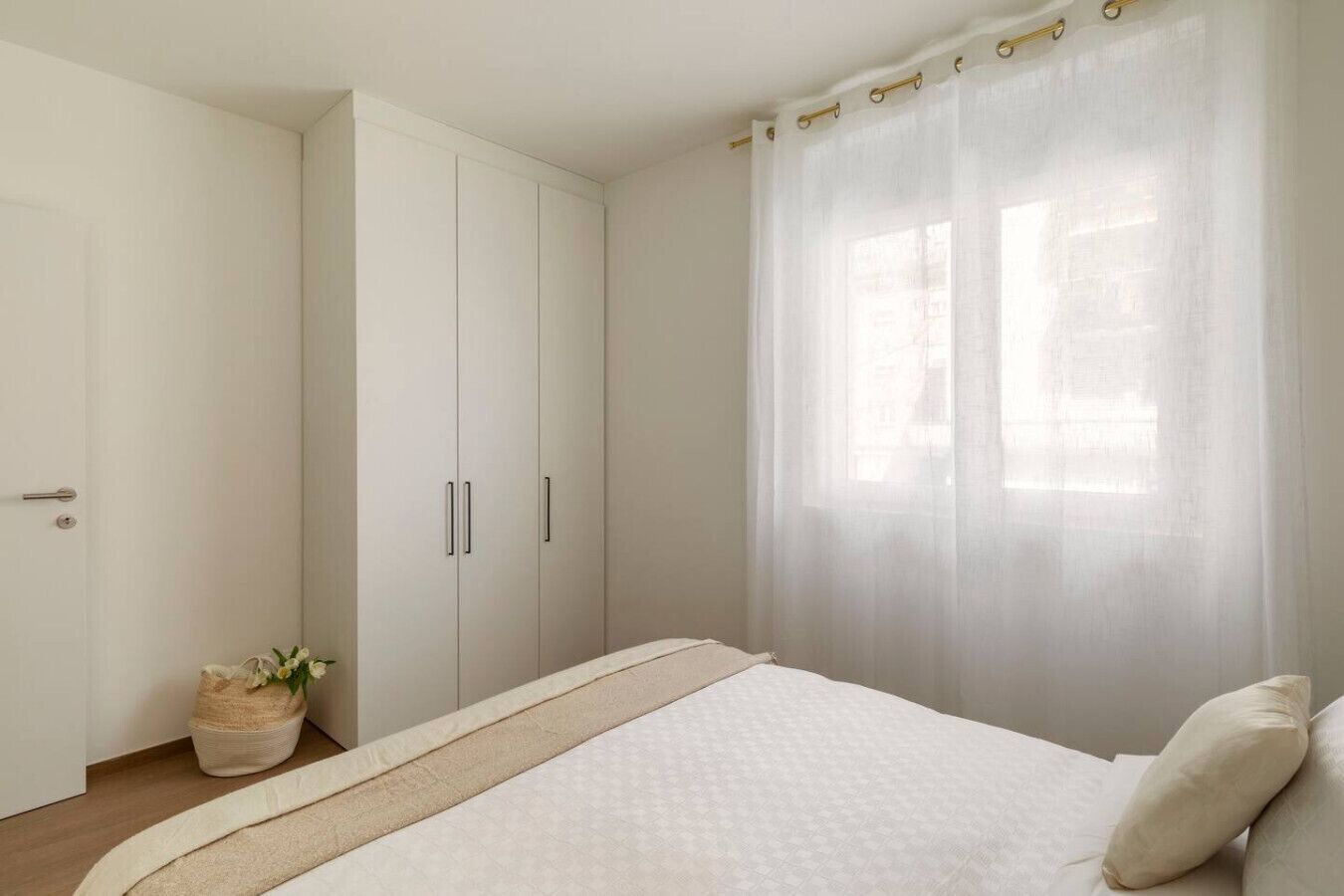 A bedroom with a bed, a wardrobe, and a window with sheer curtains.