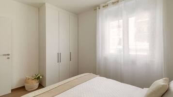 A bedroom with a bed, a wardrobe, and a window with sheer curtains.