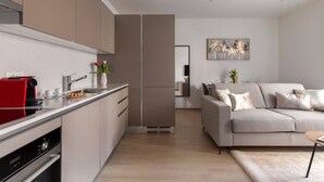 Una cucina moderna con una macchina da caffè rossa, un lavello e un vaso di fiori. Si nota un divano beige e un quadro appeso al muro.