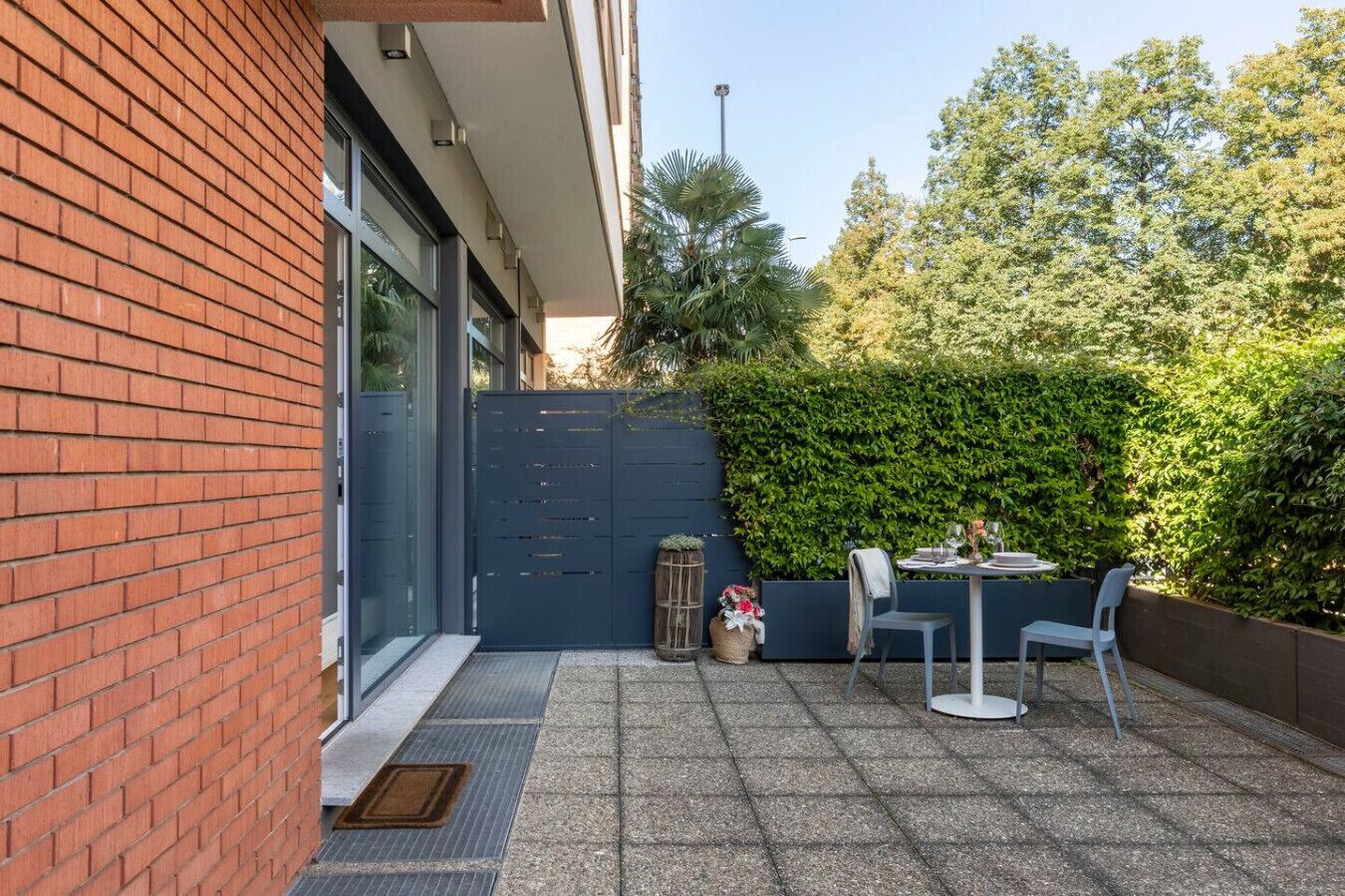 Un patio con una mesa, sillas, una cerca azul y un muro de ladrillo.