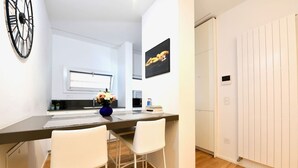 Een moderne keuken met een centraal eiland, witte stoelen, een vaas met bloemen en een klok aan de muur.