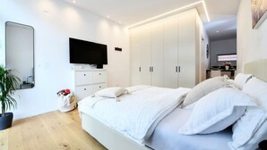 Een moderne slaapkamer met een groot bed, een aan de muur bevestigde televisie en een inloopkast.