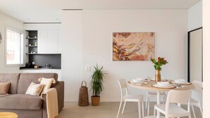 A modern living room with a sofa, dining table, chairs, and a kitchen area with cabinets and a countertop.