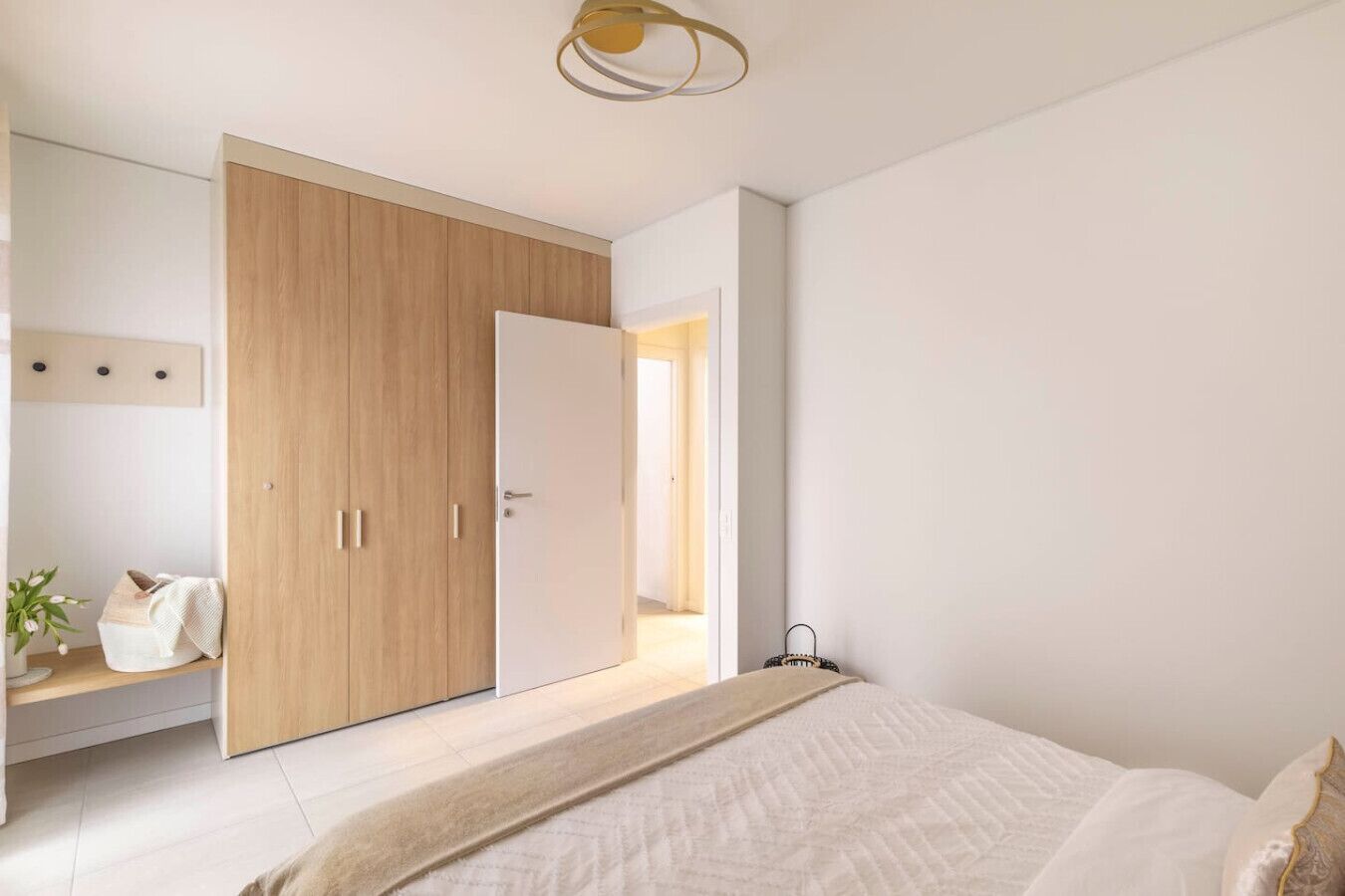 Une chambre moderne avec un grand lit, une armoire en bois et un petit coin salon agrémenté d’une plante.