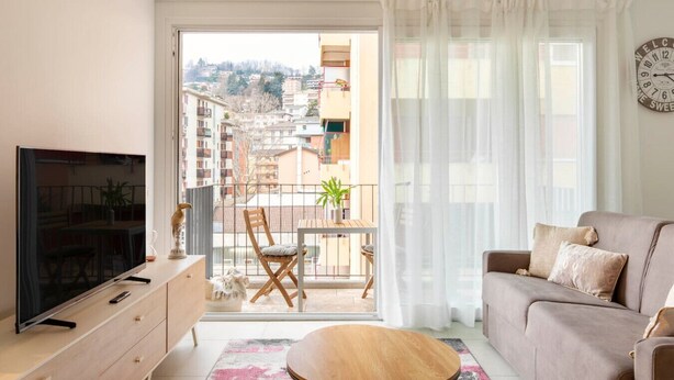 A living room with a TV, sofa, and balcony with a table and chairs.