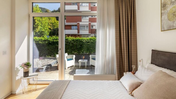 A bedroom with a large sliding glass door leading to an outdoor seating area. - Blue Diamond - Gorgeous lakefront apartment with parking (Lugano)