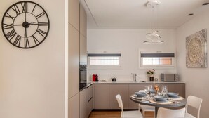 A modern kitchen with a round dining table, white chairs, and a large wall clock. - Blue Diamond - Gorgeous lakefront apartment with parking (Lugano)