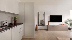 Une cuisine moderne avec des armoires blanches, un comptoir noir et une petite plante. Il y a un miroir au mur, une télévision et une armoire grise sur laquelle est posée une plante.