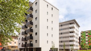 Un immeuble d’appartements moderne doté de nombreux balcons, d’un espace de stationnement et donnant sur la rue.