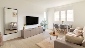 Un salon moderne doté d’un téléviseur à écran plat, d’un canapé, d’une table à manger avec des chaises et d’un grand miroir.