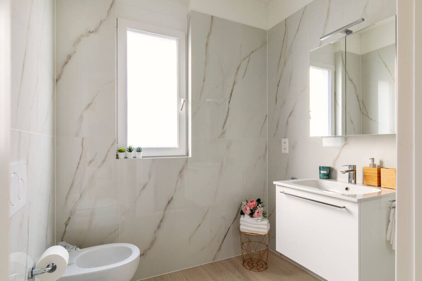 Ein modernes Badezimmer mit Marmorwand, Fenster, Waschbecken und Toilette.