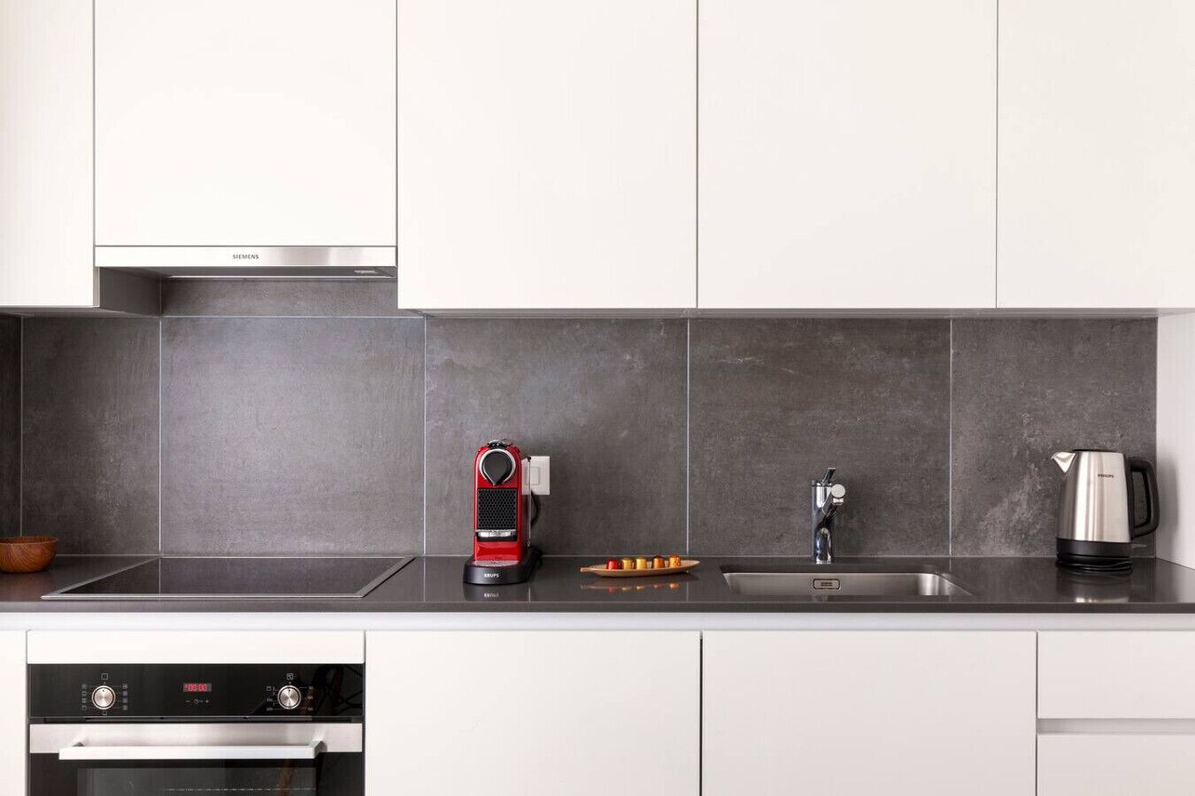 Een moderne keuken met een inbouwoven, een koffiezetapparaat, een waterkoker en een spoelbak.