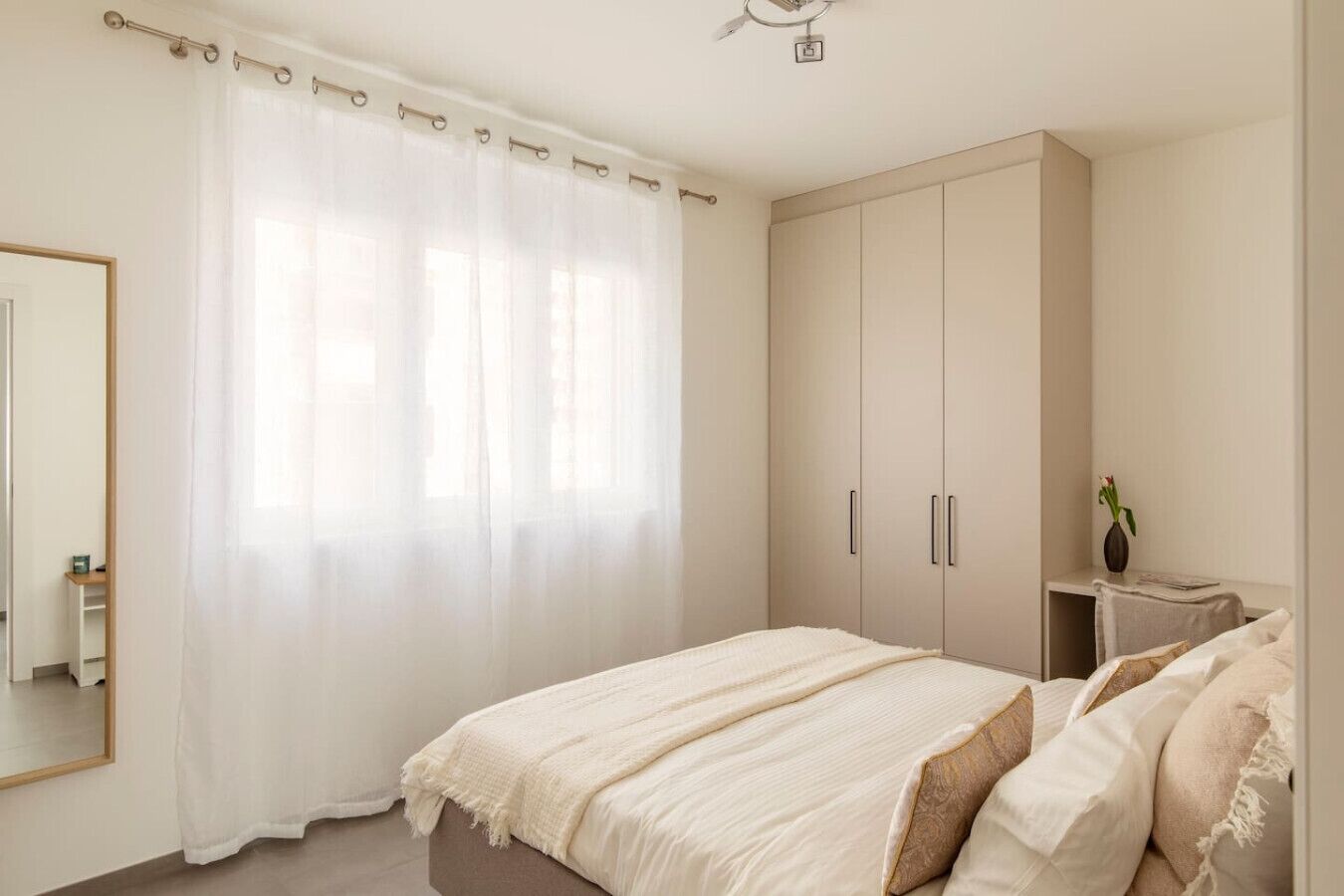 A bedroom with a bed, a wardrobe, a bedside table, and a mirror.