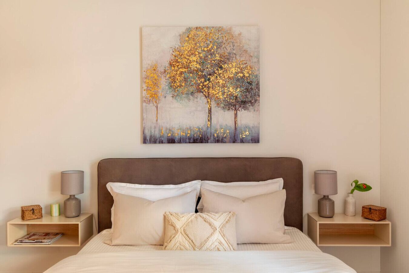A bedroom with a bed, two nightstands, a painting, and a night lamp on each side.