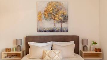 A bedroom with a bed, two nightstands, a painting, and a night lamp on each side.