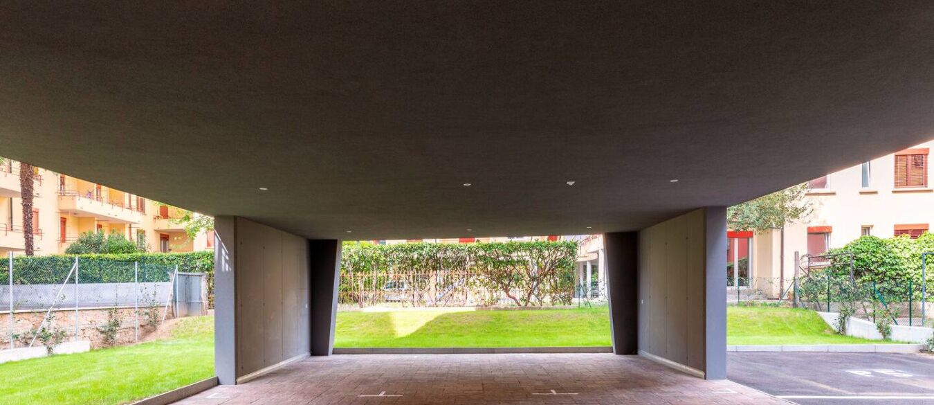 A covered outdoor area with a paved floor, surrounded by buildings and greenery.