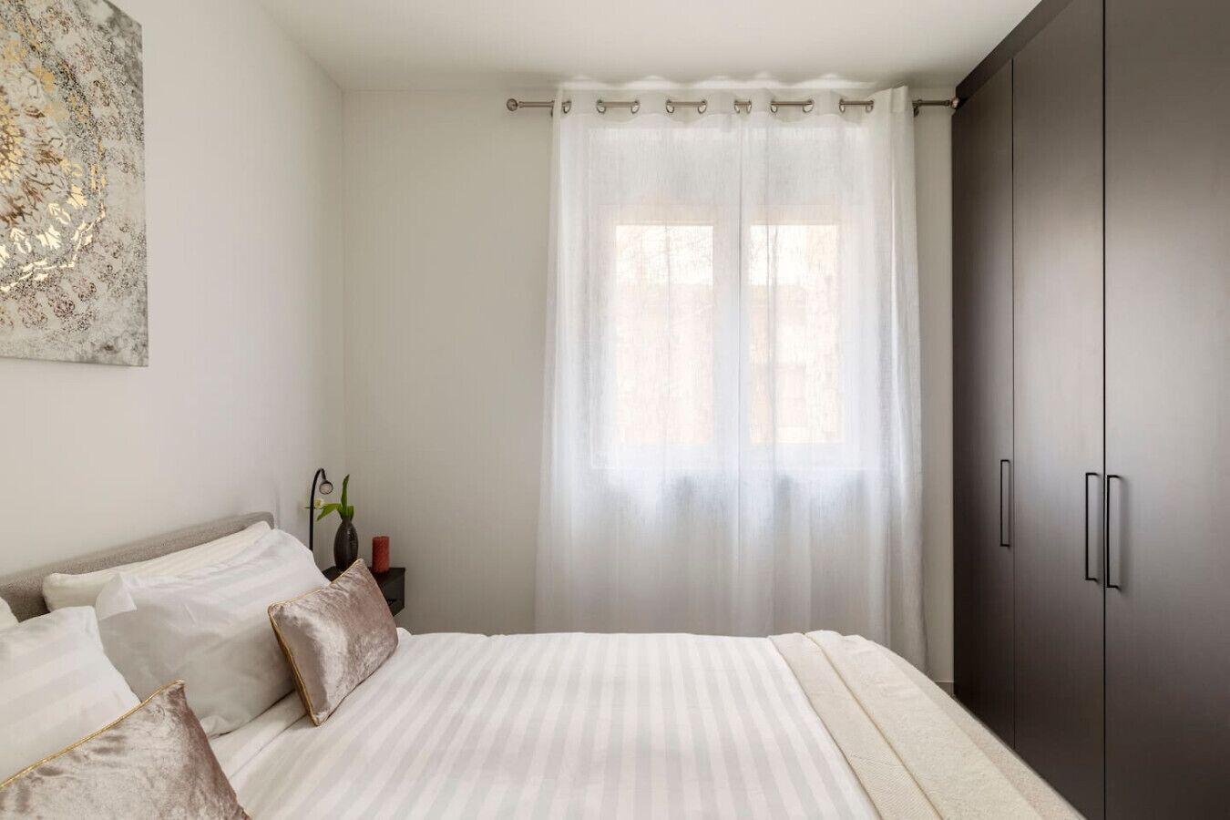 Ein Schlafzimmer mit Bett, Nachttisch, Lampe, einer Vase mit Blumen und einem Kleiderschrank.
