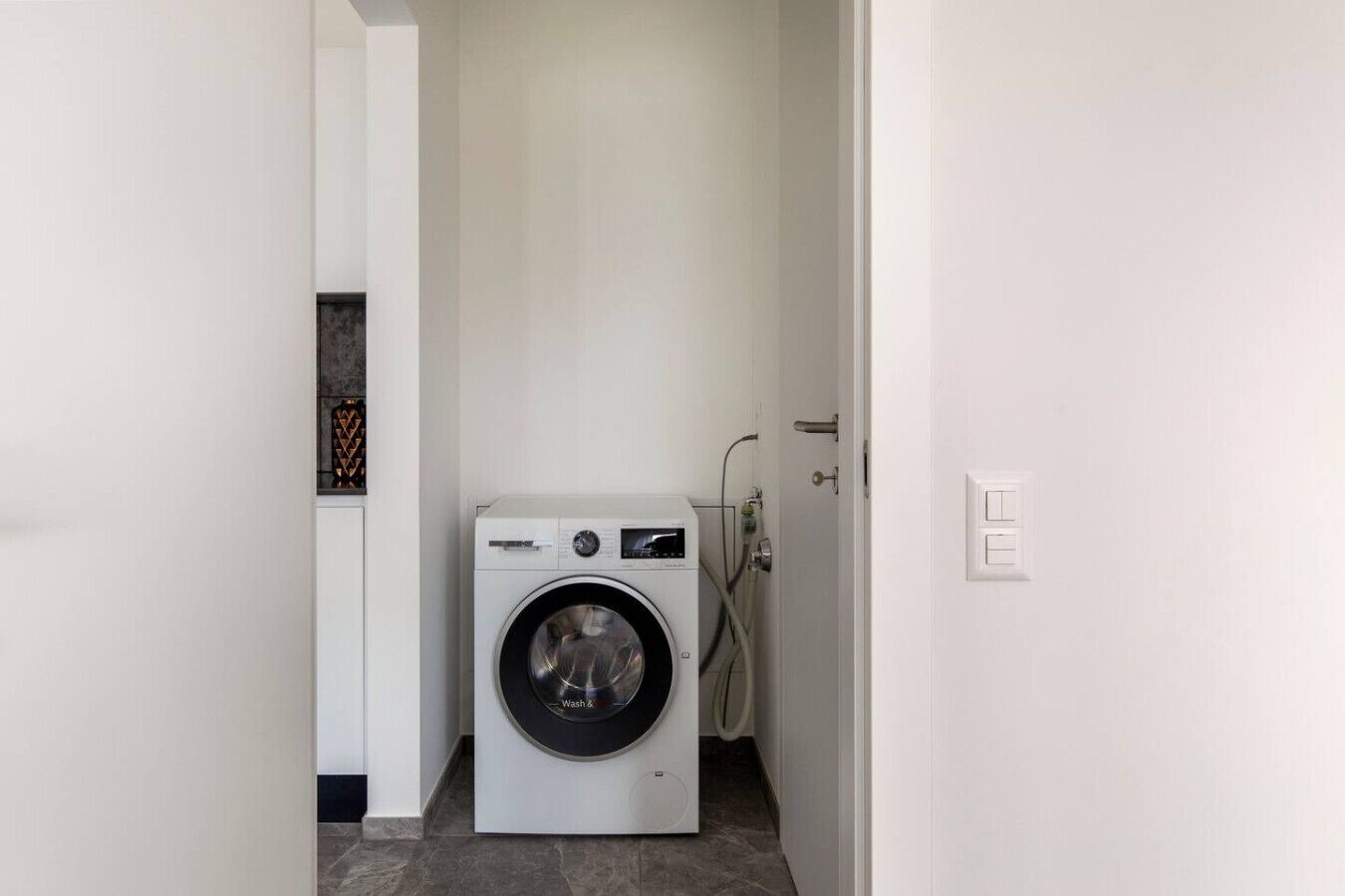 Een kleine wasruimte met een voorlader wasmachine, een deur en een betegelde vloer.