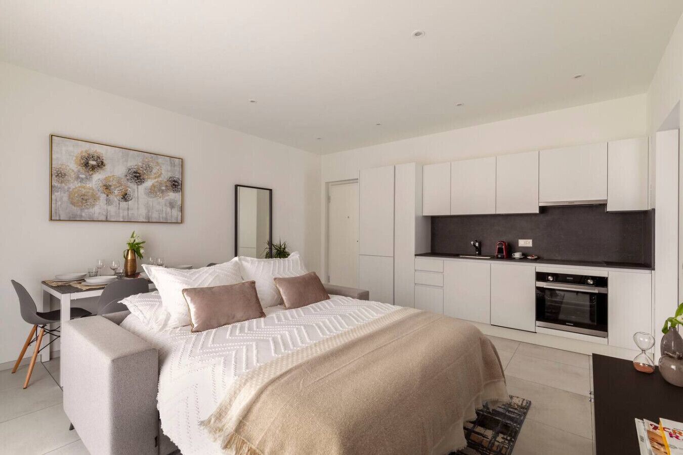A modern bedroom with a bed, bedside tables, and a small kitchenette.