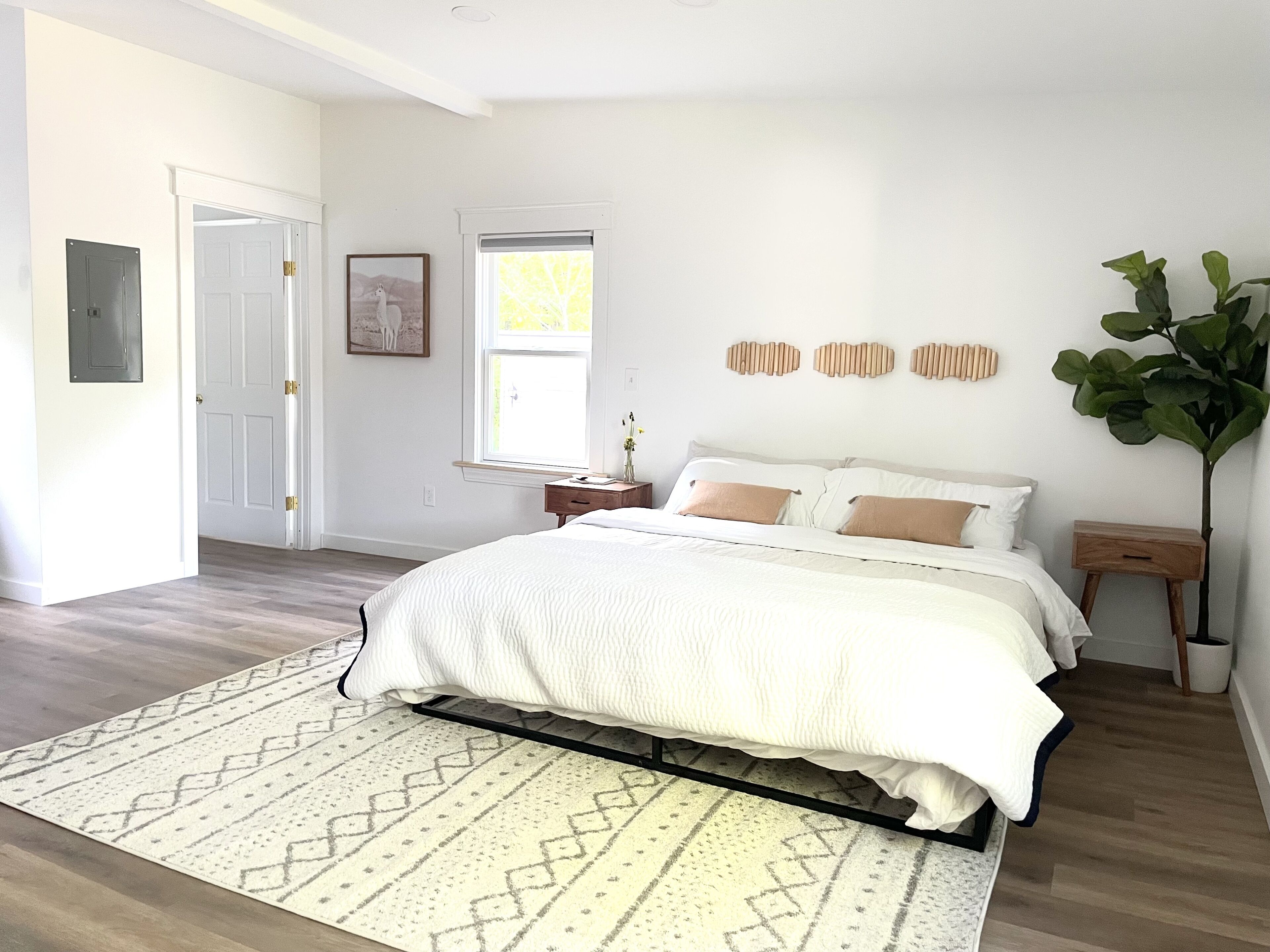 A bedroom with a bed, a nightstand, a bedside table, a window, and a door.