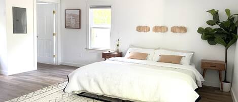 A bedroom with a bed, a nightstand, a bedside table, a window, and a door.