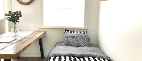 Un dormitorio con una cama de madera, un reloj de pared, una ventana y un pequeño estante con libros y una calabaza.