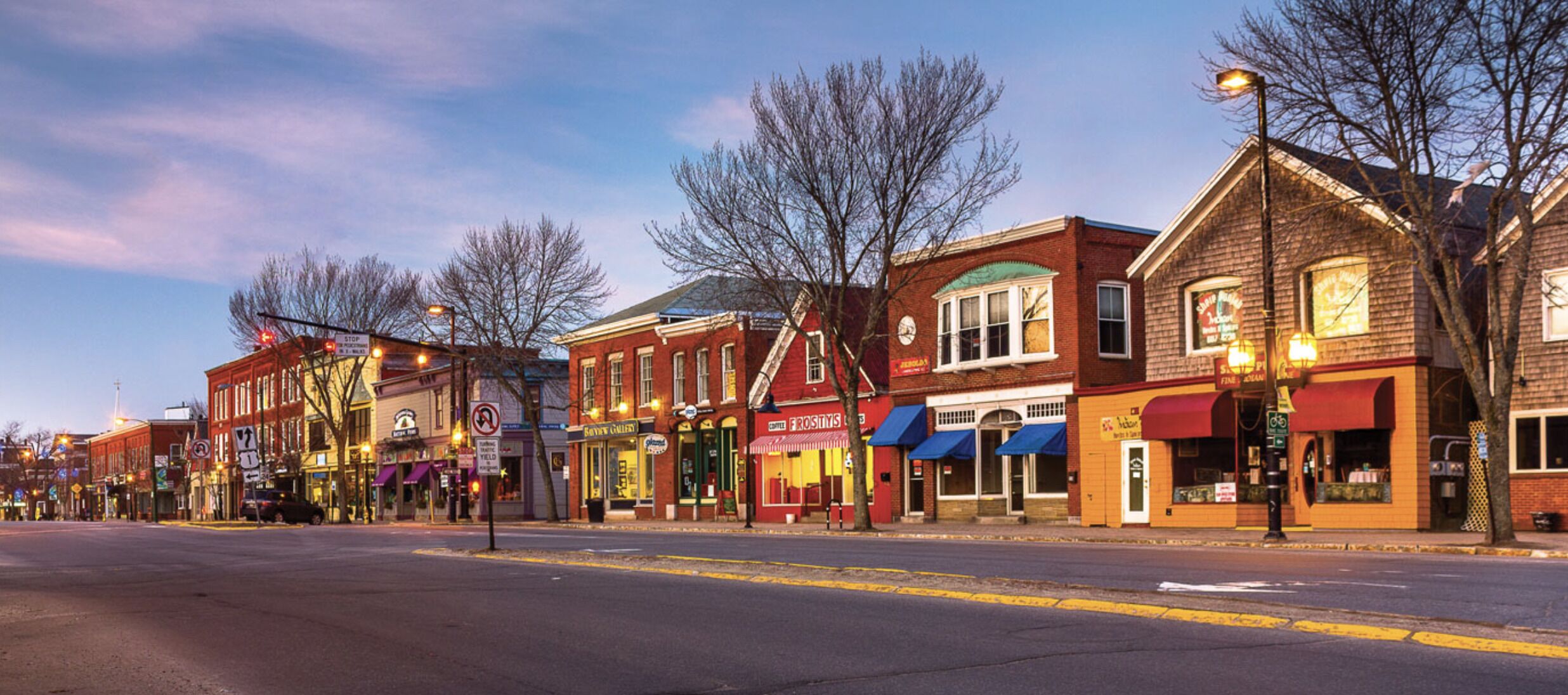A street lined with historic buildings, some with storefronts and signage, under a twilight sky.