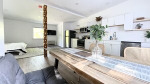 A modern kitchen with white cabinets, a stainless steel refrigerator, and a dining area with a wooden table and chairs. - King Size Sun Rise Midcoast Lovely Stay (Topsham)