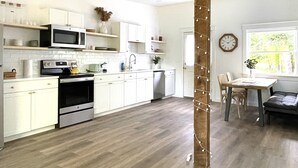 A modern kitchen with white cabinets, a microwave, stove, and a dining area with a table and chairs. - King Size Sun Rise Midcoast Lovely Stay (Topsham)