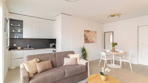 A modern living room with a sofa, a dining table, and a kitchen area with white cabinets and a black countertop. - LUNA LUX - Elegant and central apartment with parking space (Lugano)