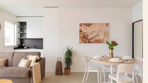 A modern living room with a sofa, a dining table set for four, and a kitchen area with a TV and shelves. - LUNA LUX - Elegant and central apartment with parking space (Lugano)