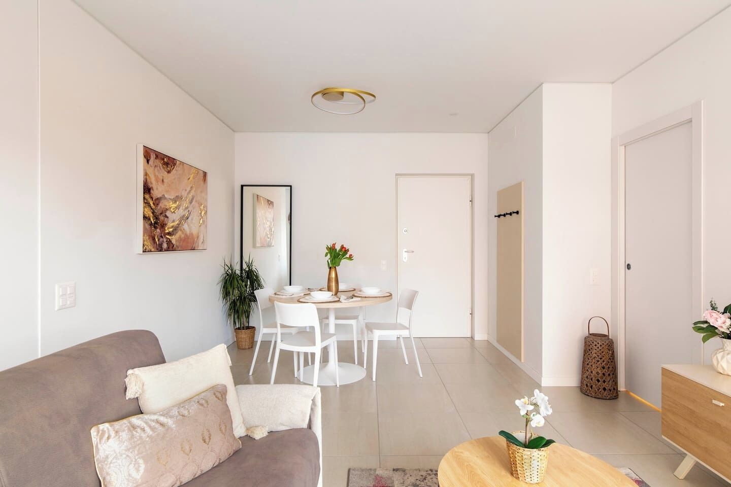 Un salon moderne avec un canapé, une table à manger et des chaises. On peut voir une plante et un vase rempli de fleurs sur la table.