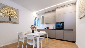 Una cucina moderna con mobili bianchi, un tavolo da pranzo con sedie e un quadro raffigurante un albero al muro.