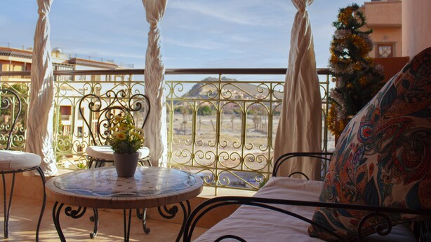 A balcony with a round table, a potted plant, and a bed with a patterned pillow. - Amoud apartments & flats (Marrakech)