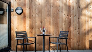 A wooden wall with a round table and two chairs, a bottle of wine, and a light fixture. - Rosthwaite  Woodland pod - a holiday Pod that sleeps 2 with an en-suite (Winster)